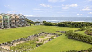 Un hotel frente al mar con un patio ajardinado y vistas al océano, además de un edificio de varios pisos con balcones.