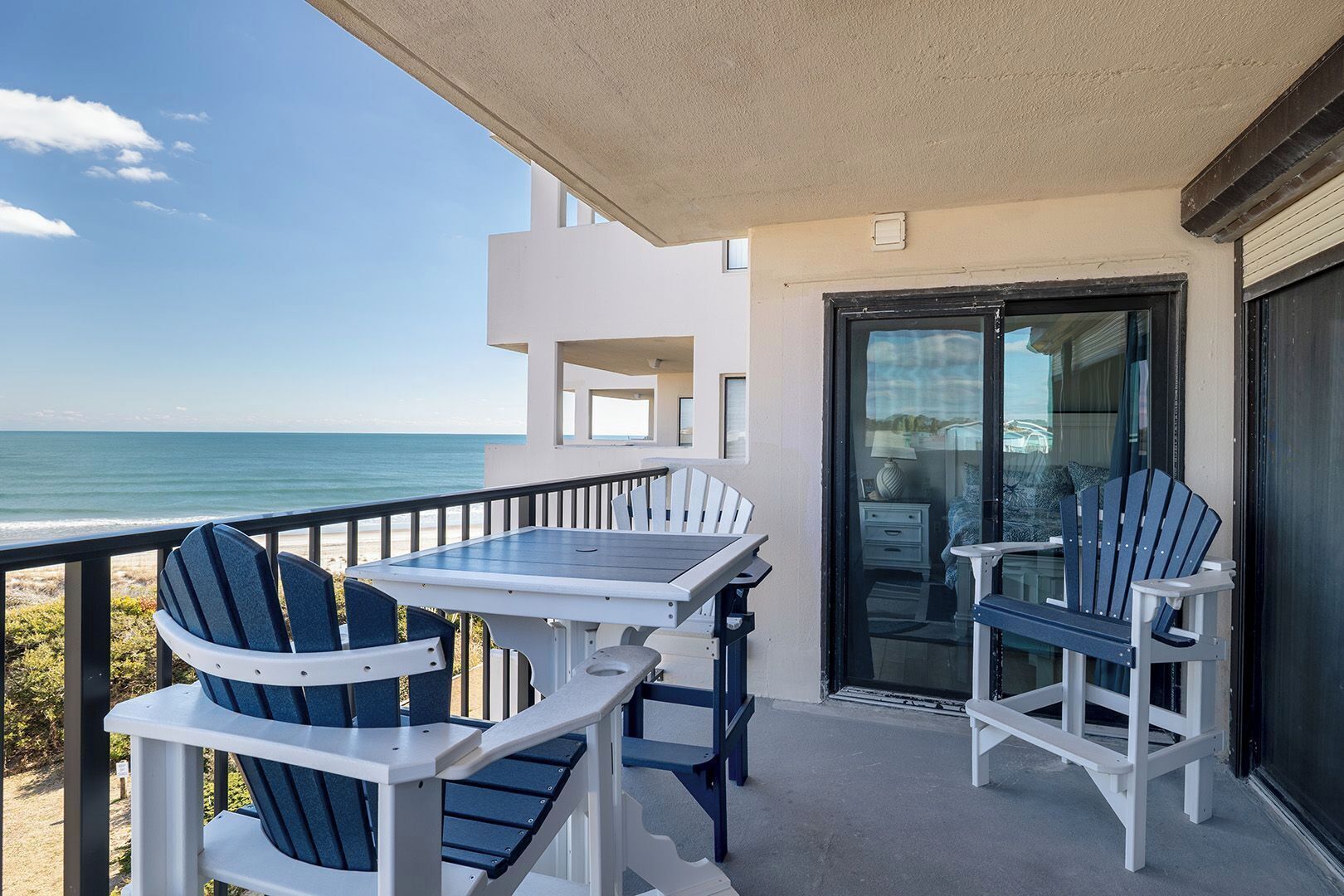 A balcony with a table and chairs, a glass door, and a view of the ocean.