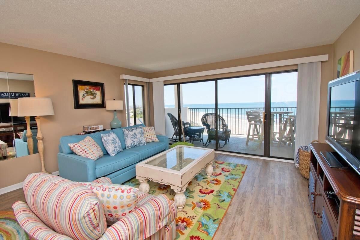 A living room with a blue sofa, striped armchairs, a glass coffee table, and a TV.