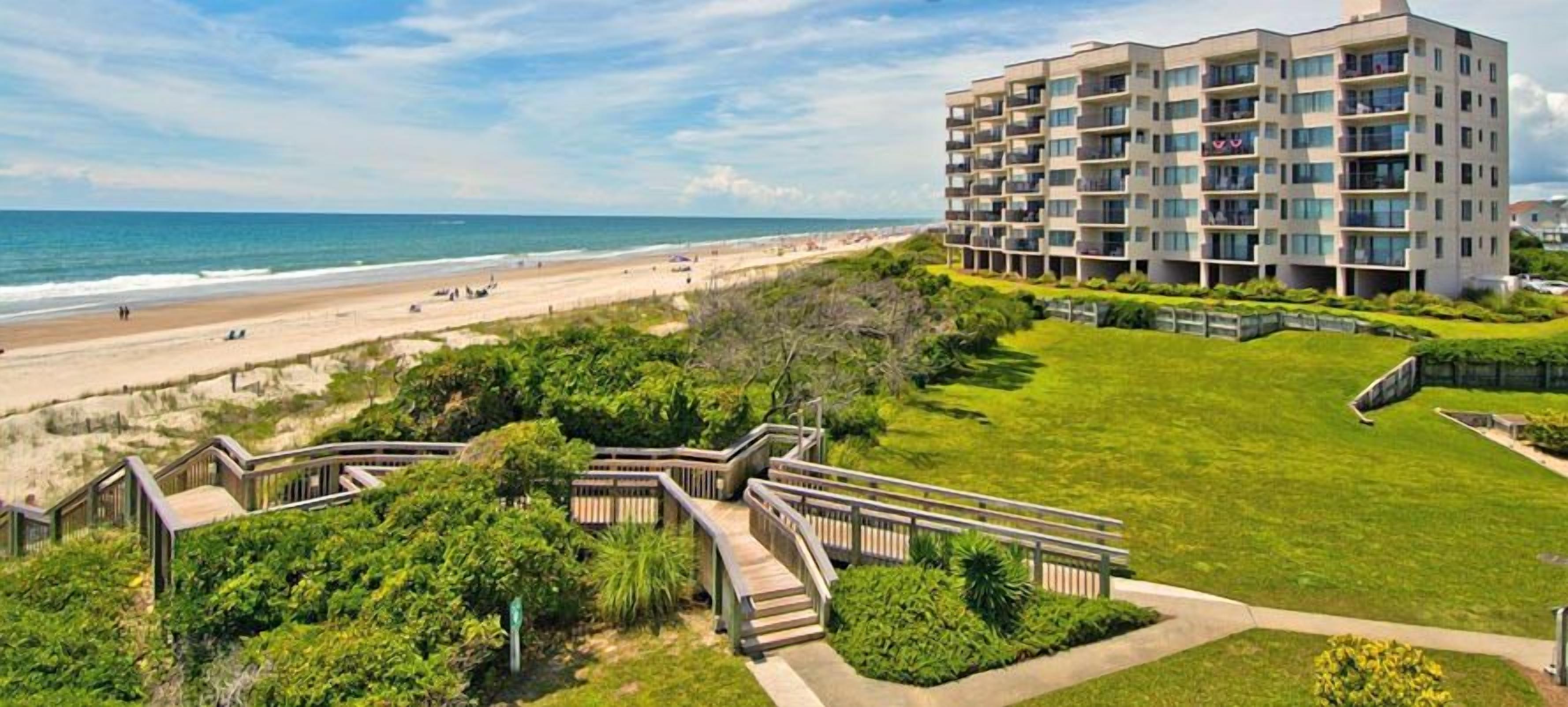 A beachfront building with multiple balconies, a well-maintained lawn, and a boardwalk leading to the beach.