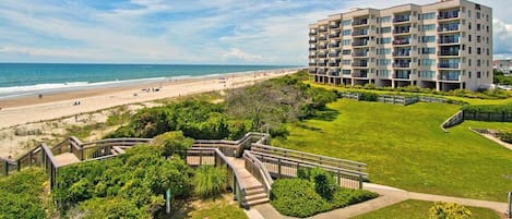 A beachfront building with multiple balconies, a well-maintained lawn, and a boardwalk leading to the beach.