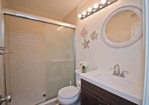 Een badkamer met een douchecabine van glas, een wit toilet, een wastafel met spiegel en decoratieve zeesterren aan de muur.