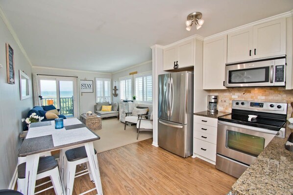 A modern kitchen with stainless steel appliances, a dining area with a table and chairs, and a view of the ocean through large windows. - Southwinds F7, Oceanfront Condo in Atlantic Beach, NC! (Atlantic Beach)