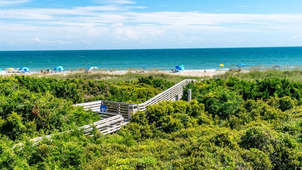 A beach with a wooden walkway leading to the shore, surrounded by dense greenery. - Southwinds F7, Oceanfront Condo in Atlantic Beach, NC! (Atlantic Beach)