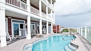 A swimming pool with a deck, lounge chairs, and a covered area with a railing. - Spindrift, Oceanfront House in Emerald Isle, NC! (Emerald Isle)