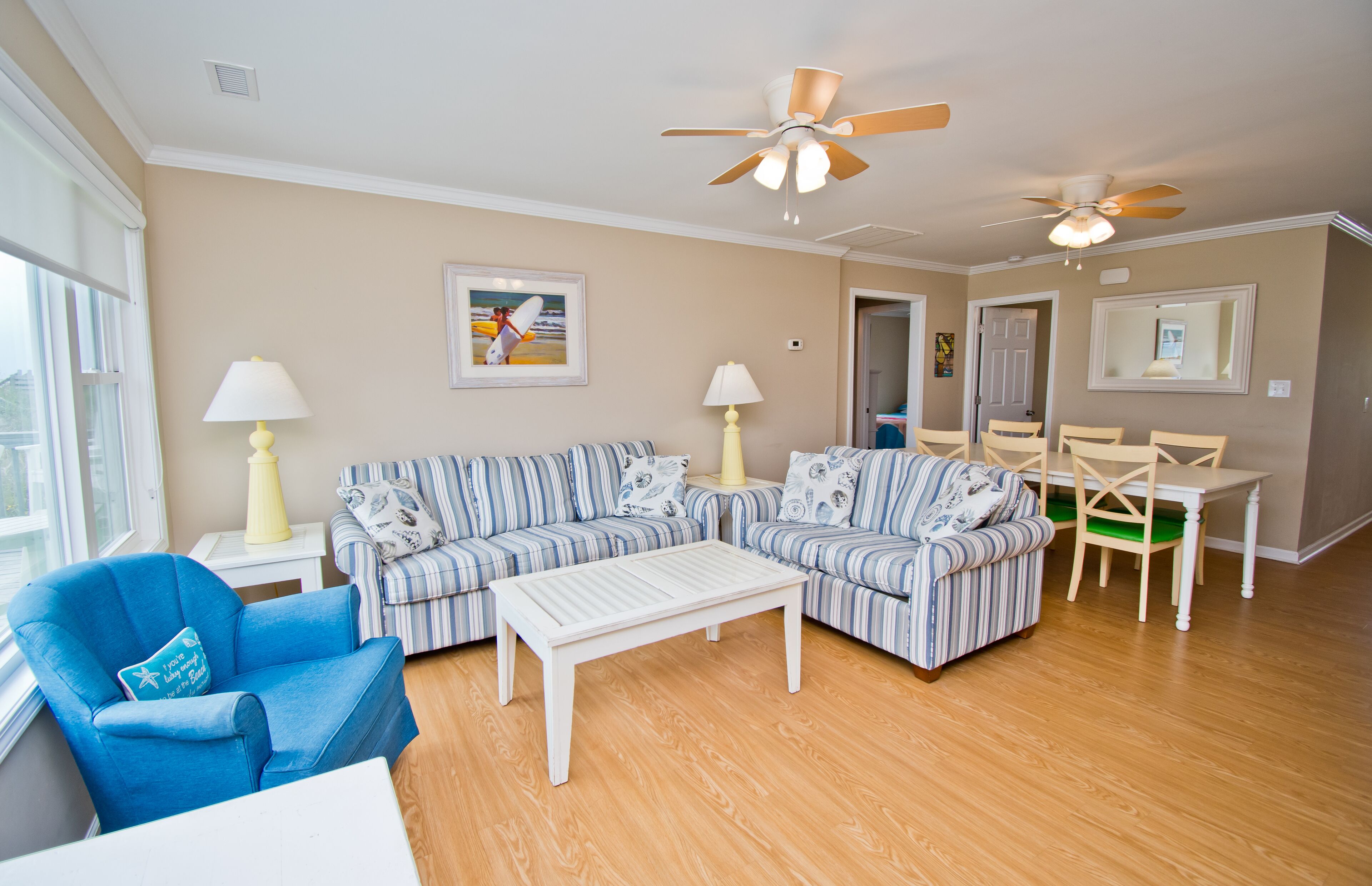 A living room with striped sofas, a coffee table, a blue armchair, and a dining table with chairs.