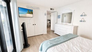 A bedroom with a bed, a TV, a dresser, and a mirror. - Summer Winds C-128, Oceanfront Condo in Indian Beach, NC! (Indian Beach)