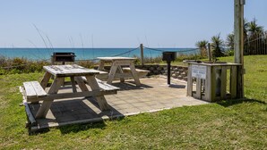 Un espace de pique-nique équipé de bancs et d’un barbecue, situé près d’une étendue d’eau.