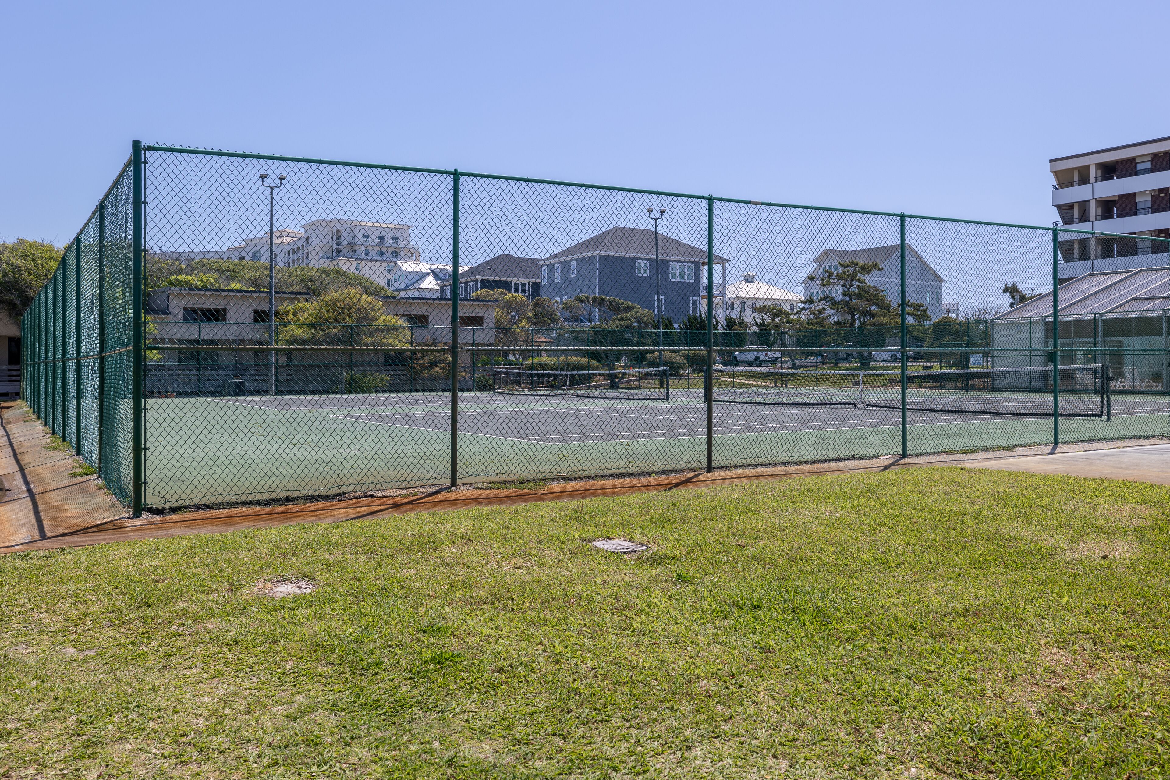 A fenced tennis court with a clear sky and buildings in the background.