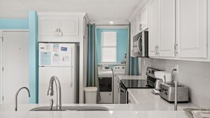 A kitchen with white cabinets, a stainless steel sink, a refrigerator, a stove, a microwave, and a toaster. - Summer Winds 221, Oceanfront Condo in Indian Beach, NC! (Indian Beach)