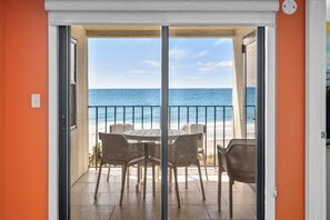 A balcony with a view of the ocean, a table, and four chairs.