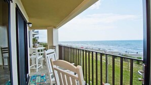 Un balcon avec vue sur la plage, des chaises blanches et une table.