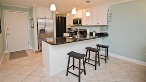 A modern kitchen with a central island, bar stools, a refrigerator, a microwave, and pendant lighting. - Summer Winds B-235, Oceanfront Condo in Indian Beach, NC! (Indian Beach)