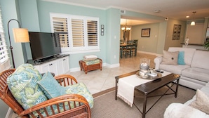 A living room with wicker furniture, a television, and a dining area with chairs and a table. - Summer Winds B-235, Oceanfront Condo in Indian Beach, NC! (Indian Beach)