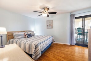 A bedroom with a bed, a ceiling fan, a window with curtains, and a view of outdoor chairs.