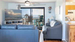 A living room with a sofa, a grey armchair, a ceiling fan, a TV, and a view of the ocean through a glass door. - Summer Winds B-237, Oceanfront Condo in Indian Beach, NC! (Indian Beach)
