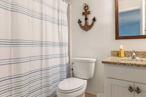 A bathroom with a striped shower curtain, a toilet, a granite countertop with a soap dispenser, and an anchor decoration on the wall.