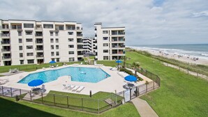 Et hotel med flere etager, en swimmingpool, udsigt til stranden og en indhegnet patio.