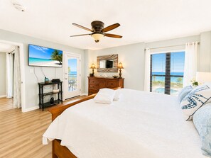A hotel room with a bed, a ceiling fan, a TV, a dresser, and a view of the ocean.