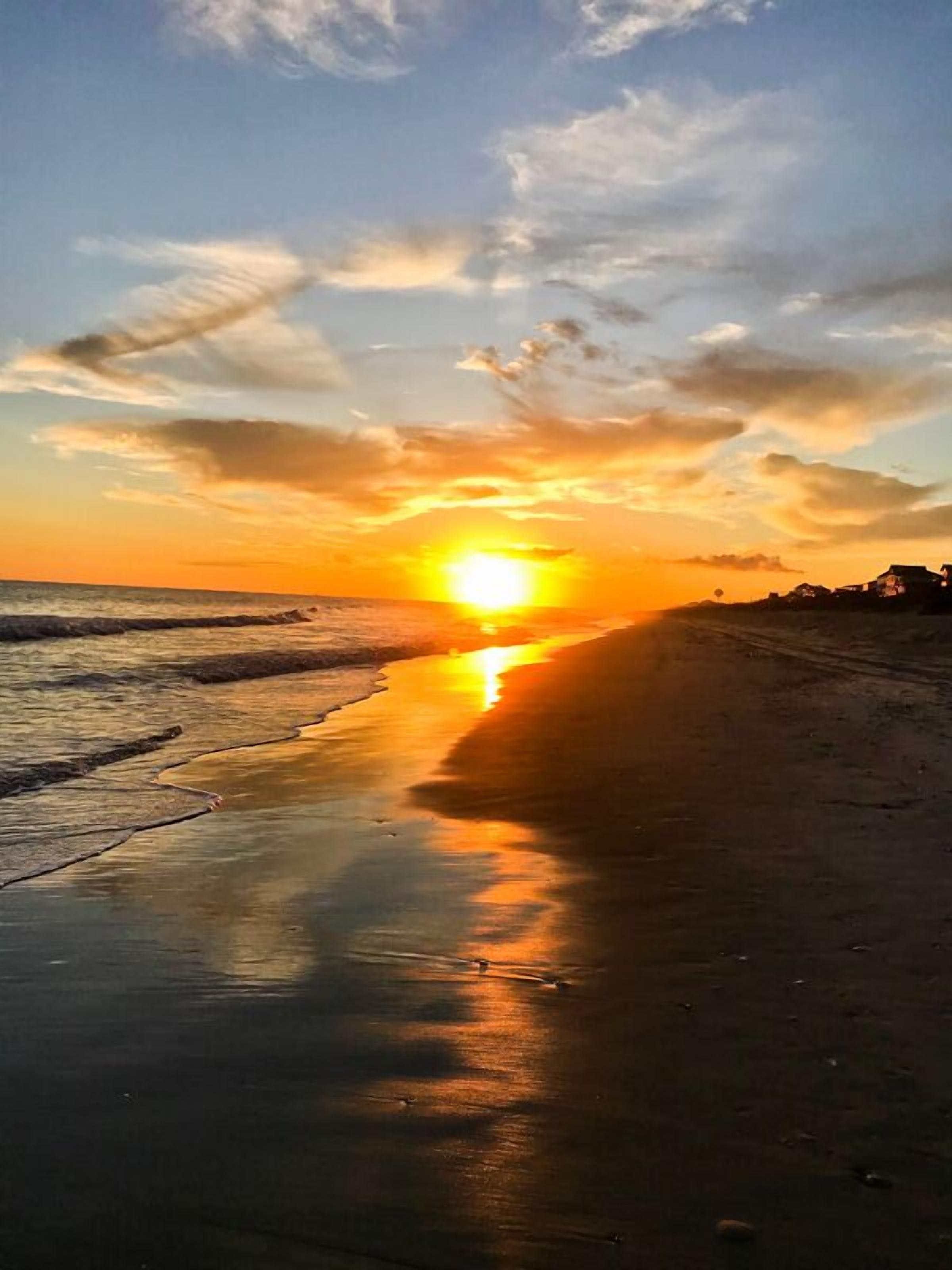 A beach at sunset with the sun reflecting on the wet sand.