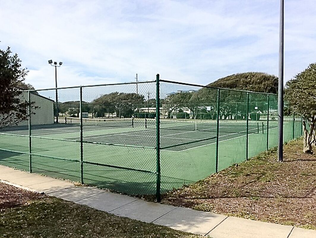 A tennis court enclosed by a chain-link fence with a building adjacent to it.