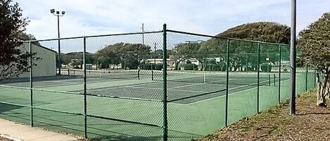 A tennis court enclosed by a chain-link fence with a building adjacent to it.