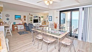Un vaste espace de vie comprenant une table à manger, des chaises, un ventilateur de plafond et une vue sur l’extérieur grâce à une porte-fenêtre coulissante.