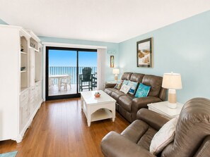 A living room with a sofa, coffee table, and a view of the balcony. - Summer Winds B-439, Oceanfront Condo in Indian Beach, NC! (Indian Beach)