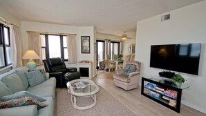 A spacious living room with a sofa, armchairs, a coffee table, and a TV. - Summer Winds A-505, Oceanfront Condo in Indian Beach, NC! (Indian Beach)