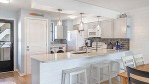 Una cocina moderna con una isla central, muebles blancos y una zona de comedor con taburetes de bar.