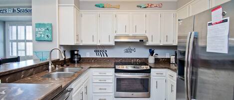 A kitchen with white cabinets, a stainless steel refrigerator, a built-in oven, and a granite countertop.