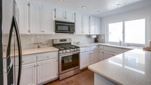 A kitchen with white cabinets, stainless steel appliances, and a large window providing natural light. - Your Spring & Summer Coastal Retreat Awaits in Huntington Beach!  (Huntington Beach)