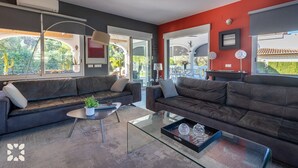 A modern living room with two dark sofas, a glass coffee table, and a large window offering a view of the outdoors. - Villa Pacifica by Abahana Villas (Javea / Xàbia)