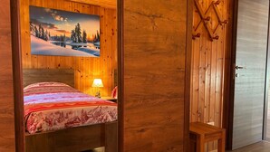 A wooden room with a bed, a nightstand, a lamp, and a door. - Apartments Les Crouses Tavern (Valtournenche)