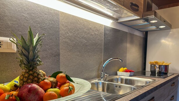 A kitchen with a stainless steel sink, a bowl of fruit, and a container of spaghetti. - Apartments Les Crouses Tavern (Valtournenche)