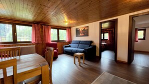 A cozy room with a wooden ceiling, a blue sofa, a wooden dining table, and a red chair. - Apartments Les Crouses Tavern (Valtournenche)
