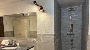 A modern bathroom with a granite countertop sink, a large mirror, and a shower with a rain showerhead. - Apartments Les Crouses Tavern (Valtournenche)