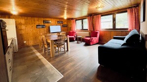 A cozy cabin interior with wooden walls, a dining area, a sofa, and a TV. - Apartments Les Crouses Tavern (Valtournenche)