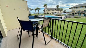 A balcony with a pool, chairs, and a view of the ocean and palm trees. - Ocean view 2 bedroom townhouse (ST. AUGUSTINE)