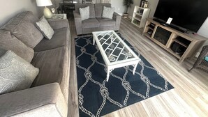 A living room with a sofa, a coffee table, a TV, and a bookshelf. - Ocean view 2 bedroom townhouse (ST. AUGUSTINE)