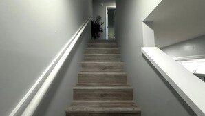 A staircase with wooden steps and white handrails, leading to a room with a white door and a plant. - Ocean view 2 bedroom townhouse (ST. AUGUSTINE)