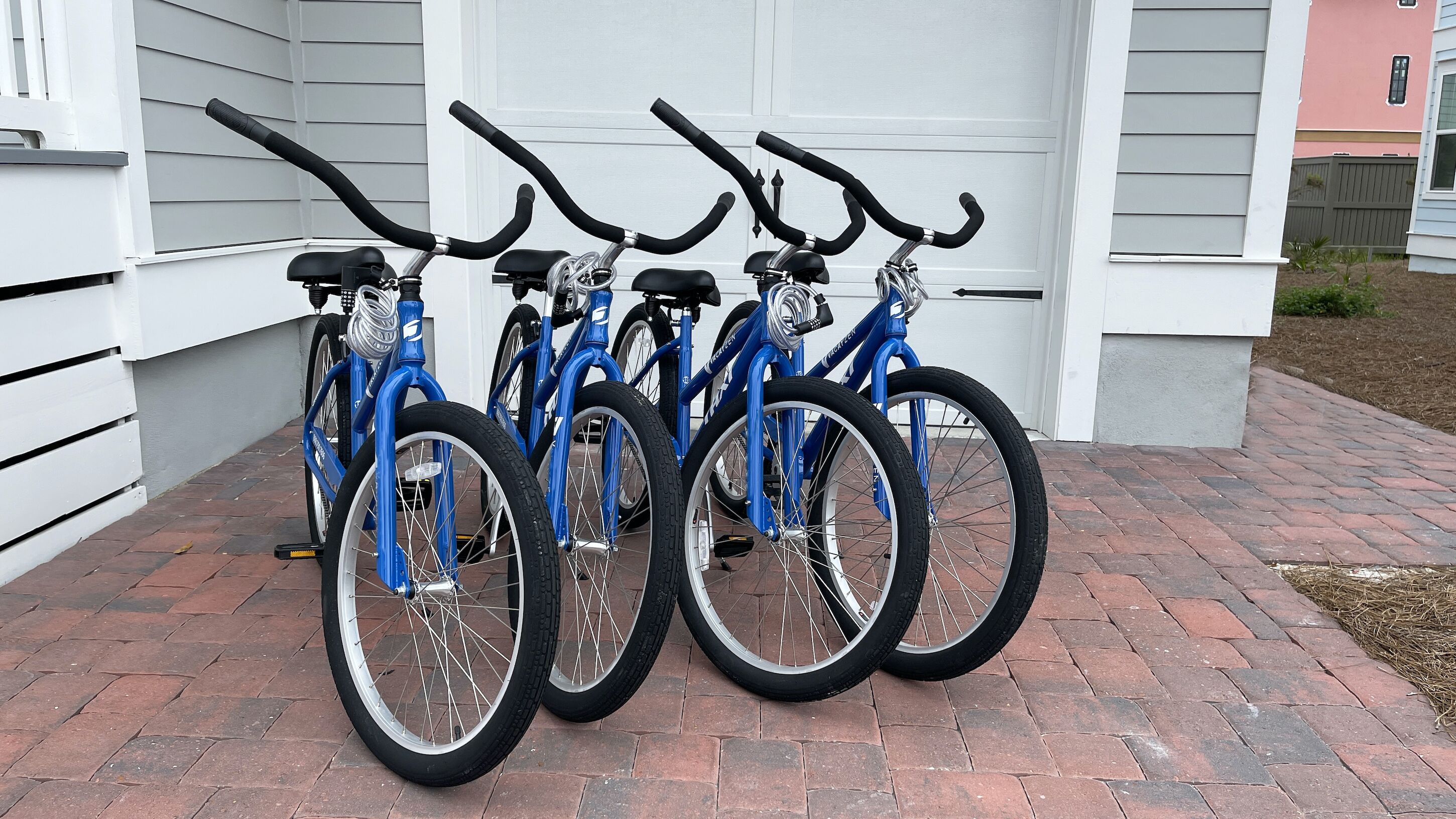 A row of blue bicycles parked in front of a white building with a garage.