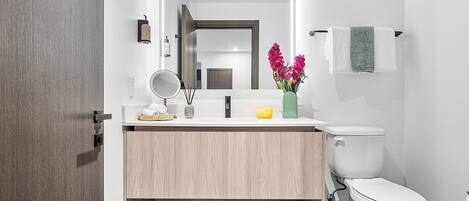 Une salle de bain moderne avec un meuble-lavabo en bois, un miroir, des toilettes et un vase rempli de fleurs.