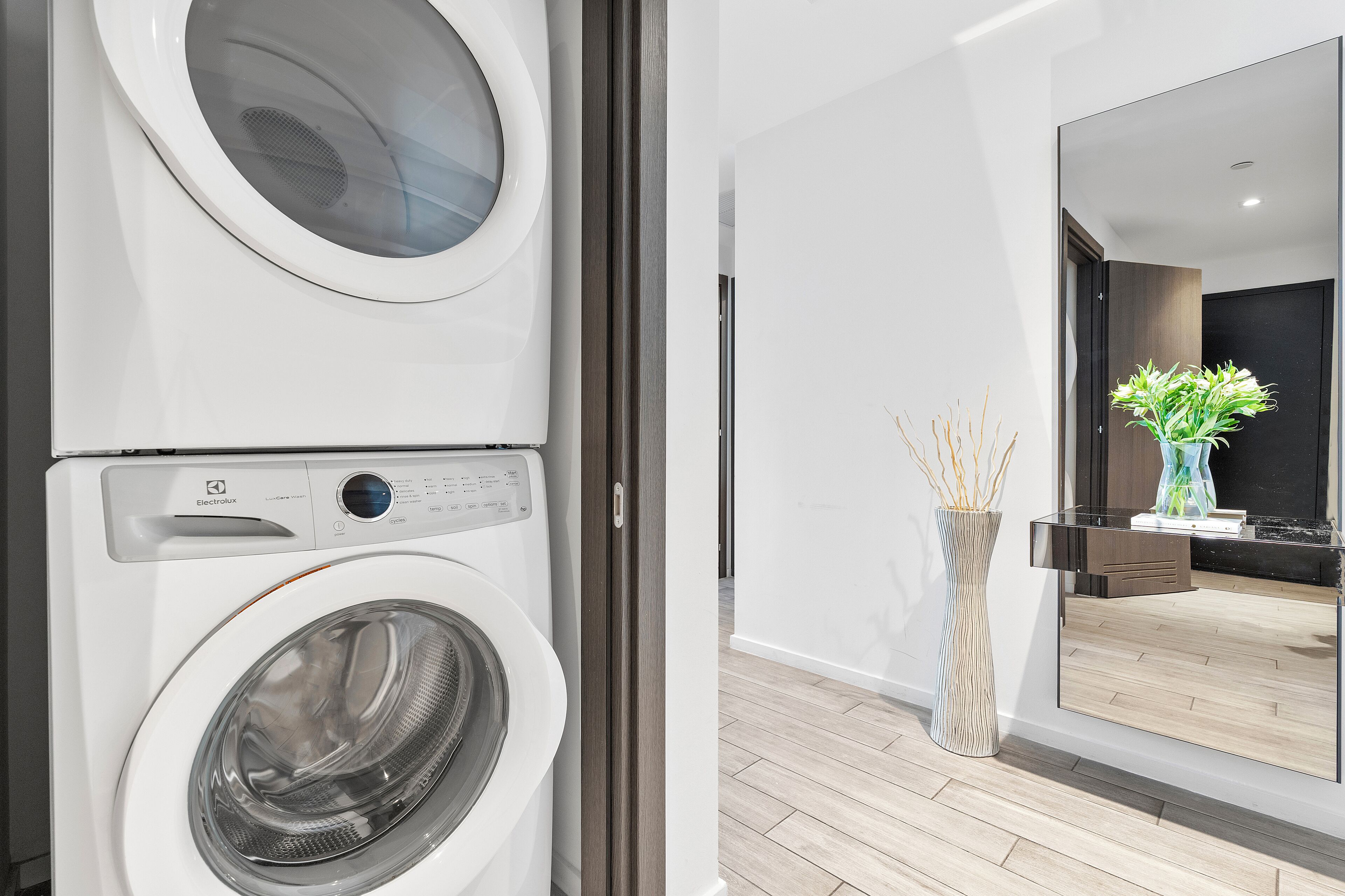 A modern laundry room with stacked washing machines and a large mirror reflecting a well-lit interior.
