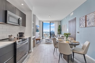 Una cocina moderna con microondas y estufa integrados, un comedor con mesa dispuesta para cuatro personas, y un ventanal con vistas a la ciudad.