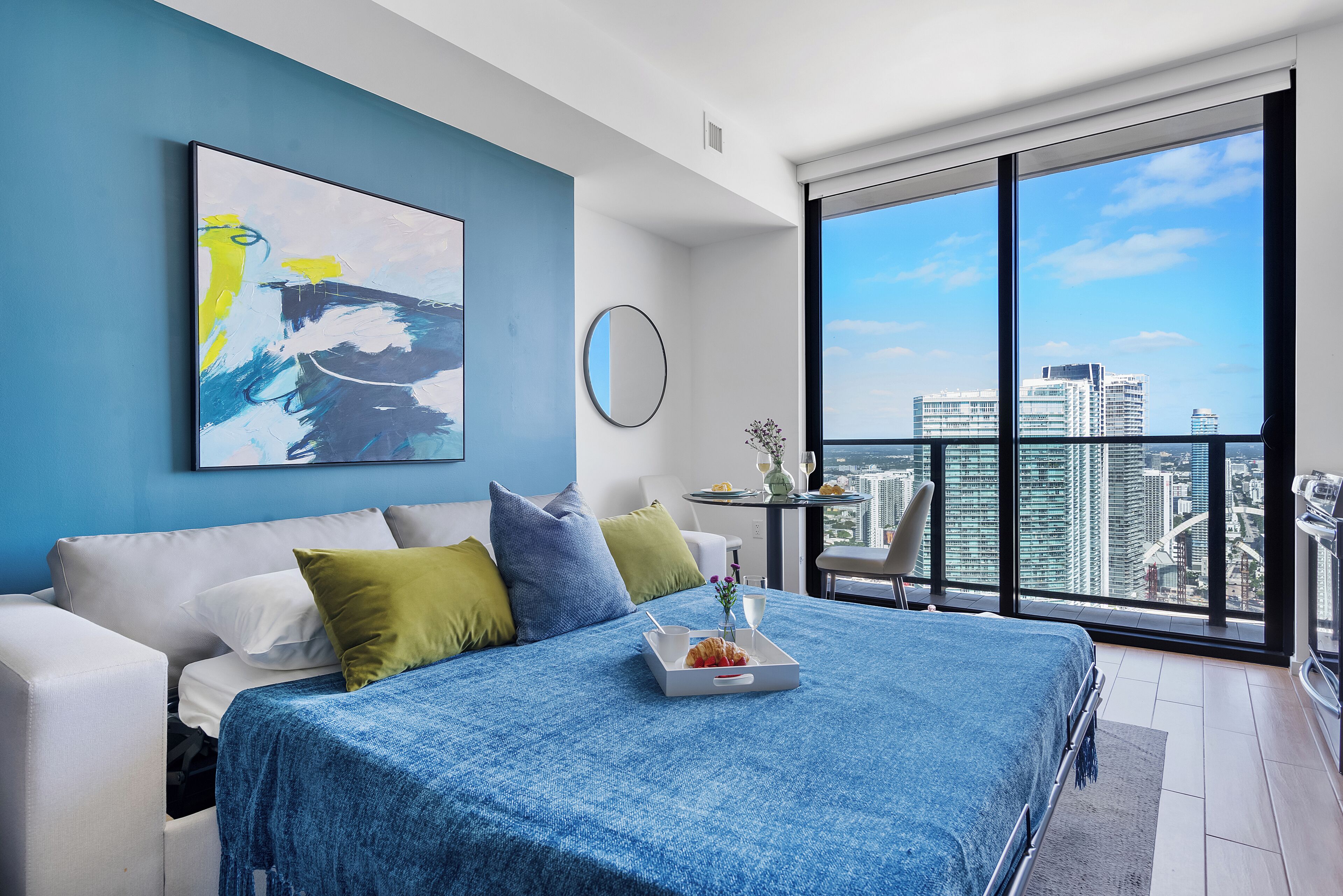 Ein modernes Schlafzimmer mit großem Bett, Blick auf die Stadt, einem Gemälde an der Wand und einer Essecke mit Tisch und Stühlen.