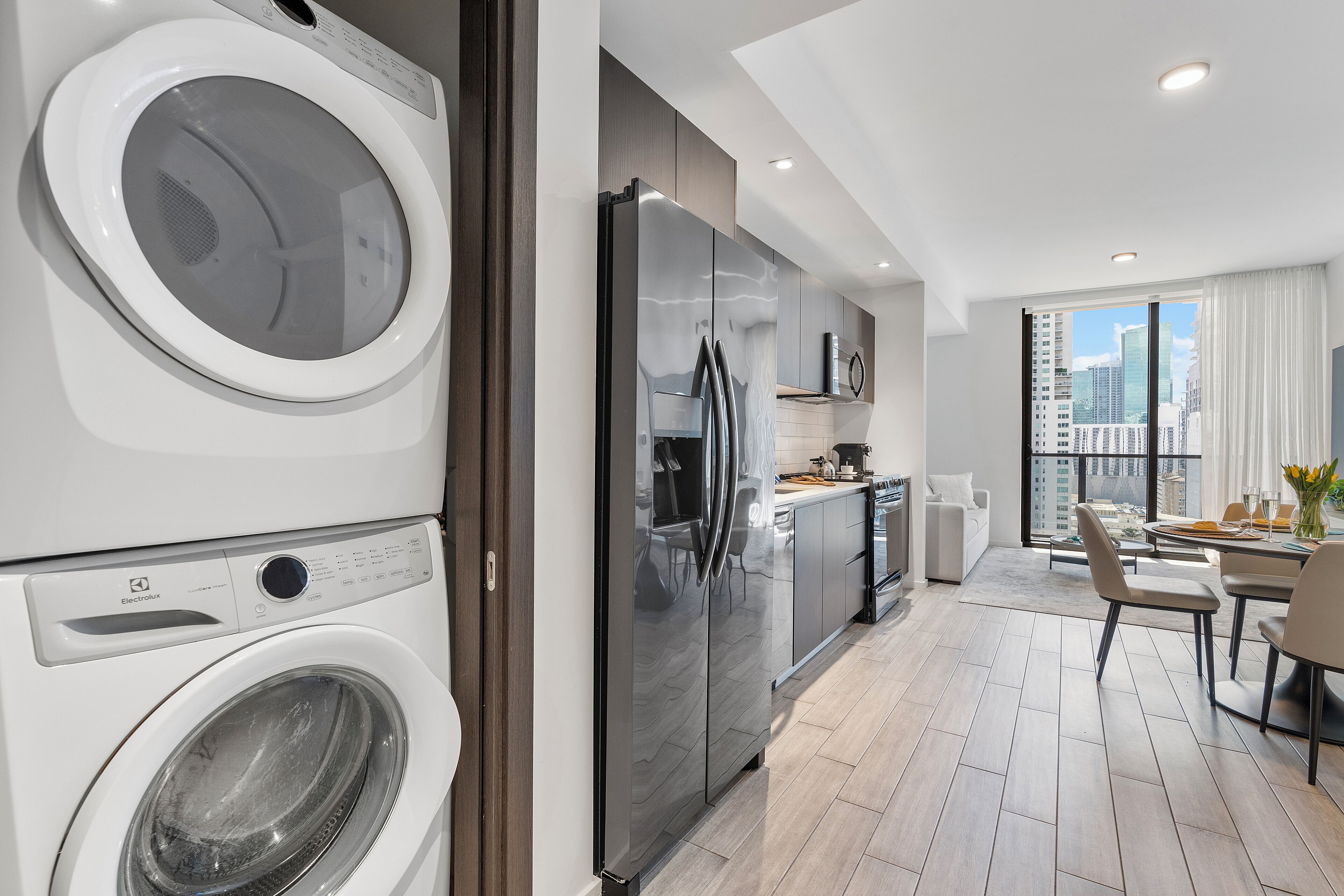 Una cucina moderna con lavatrice e asciugatrice integrate, frigorifero e zona pranzo con vista sulla città.