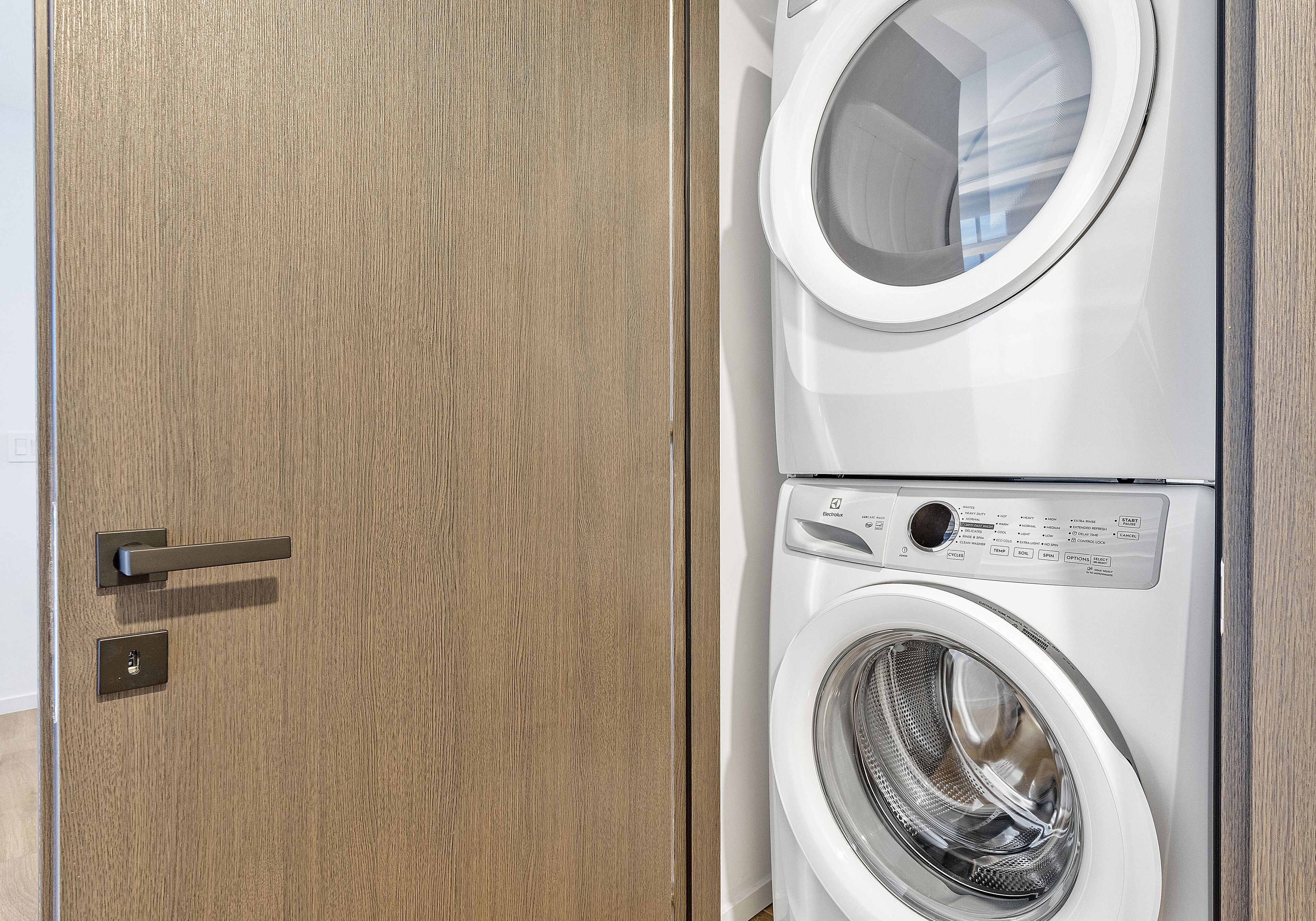 A front view of a modern laundry room with a wooden door and two stacked washing machines.