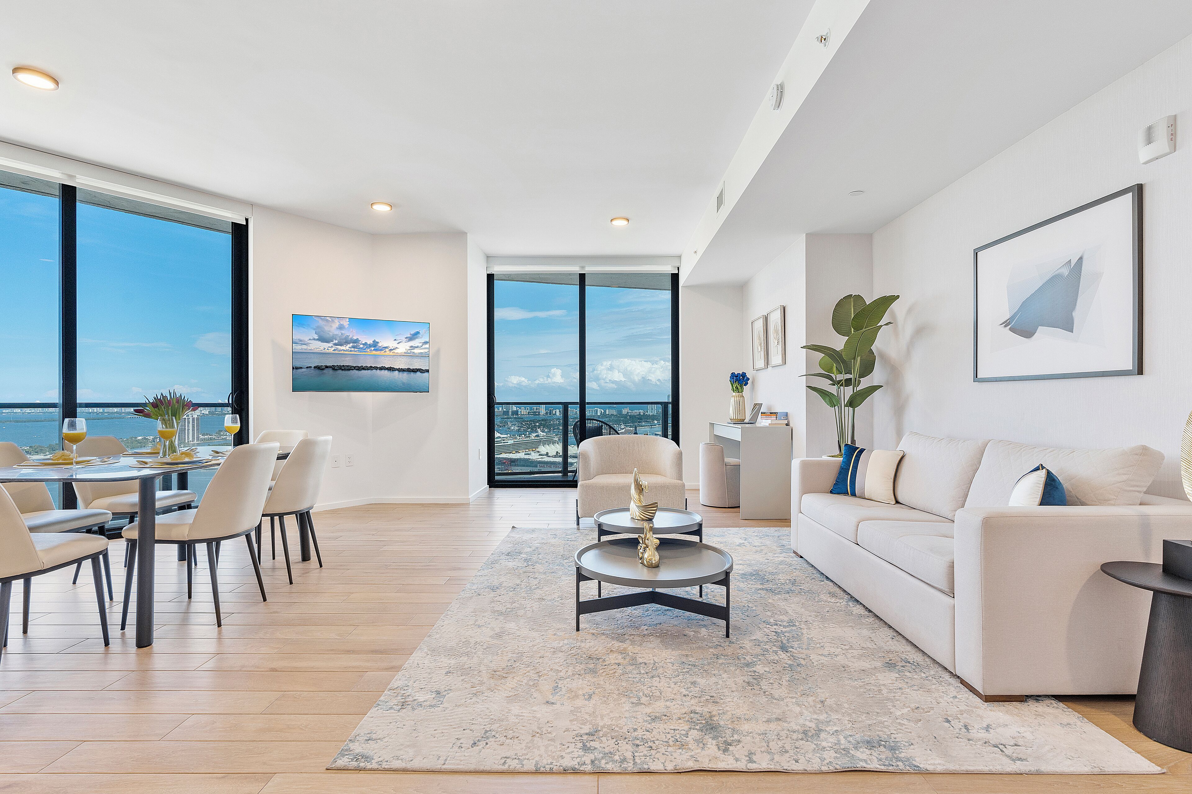 A modern living room with a dining area, large windows, and a view of the city.