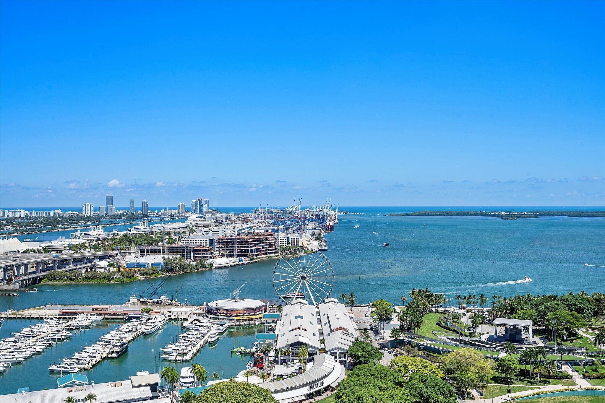 A marina with boats, a Ferris wheel, and a cityscape with buildings and a clear blue sky.